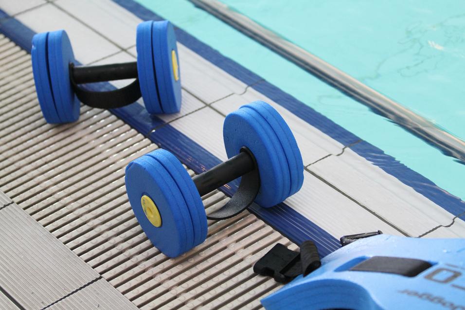 Zwei blaue Schaumstoff-Handgewichte liegen auf dem Boden am Rand eines Schwimmbeckens.